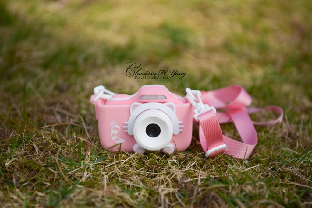 A pink children's camera laying on the grass.