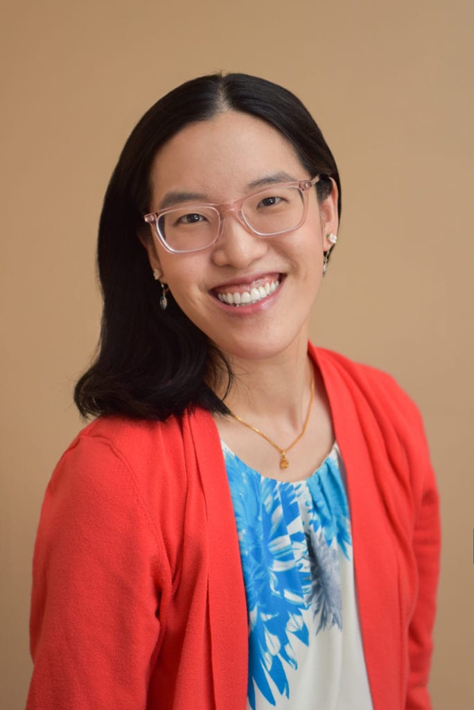 An Asian woman with red sweater and blue and white blouse smiling for her headshot.