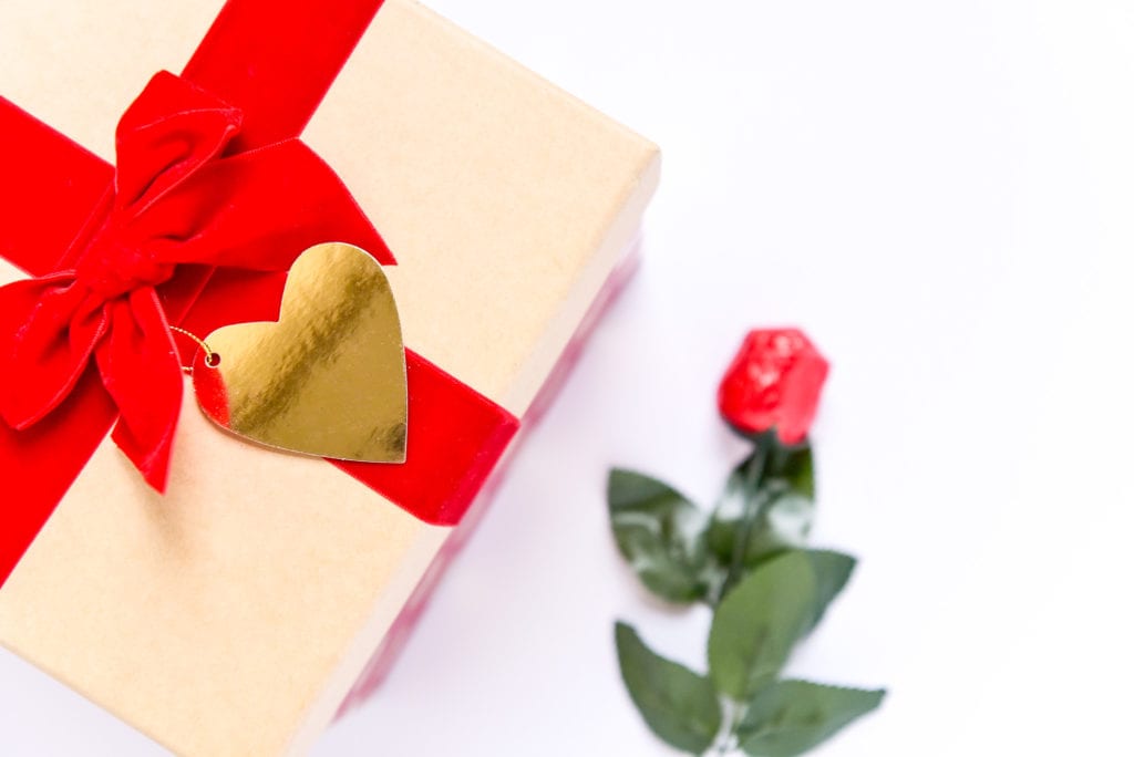A red chocolate rose and a gift box with red bow and gold heart gift tag.