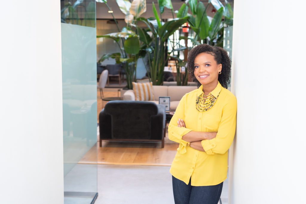 An African American woman in a yellow shirt posing with her arm crossed for her branding photoshoot.