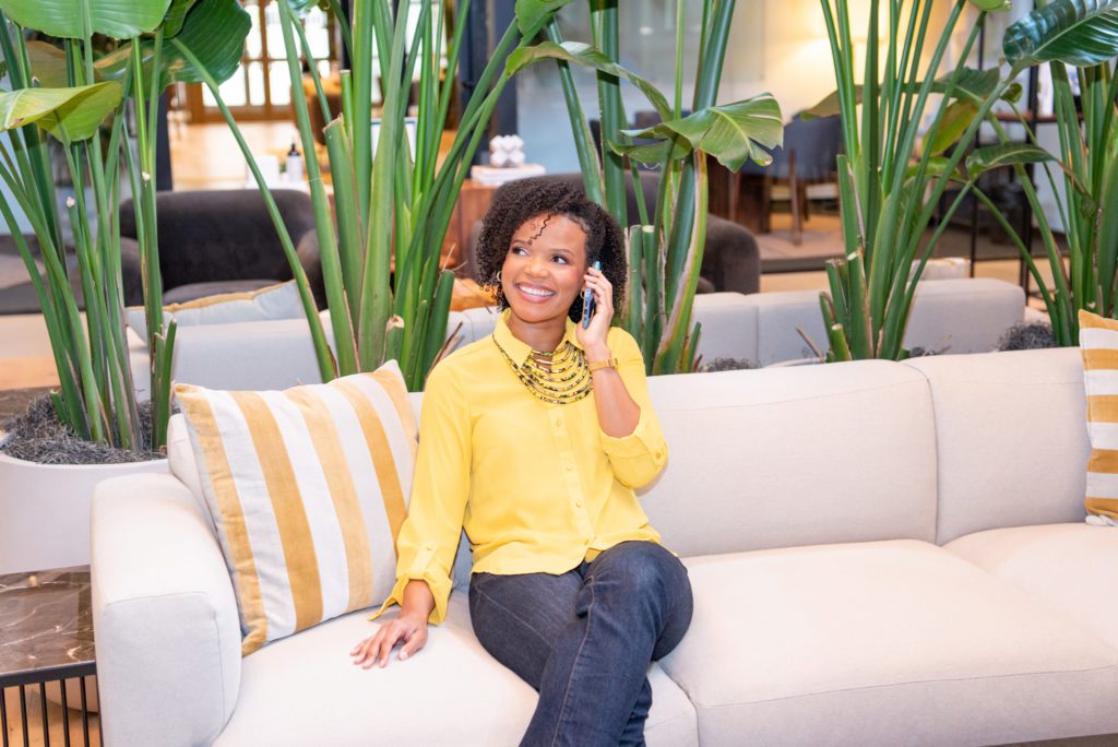 An African American lawyer wearing a bright yellow shirt talking on her phone and smiling at a co-working space.