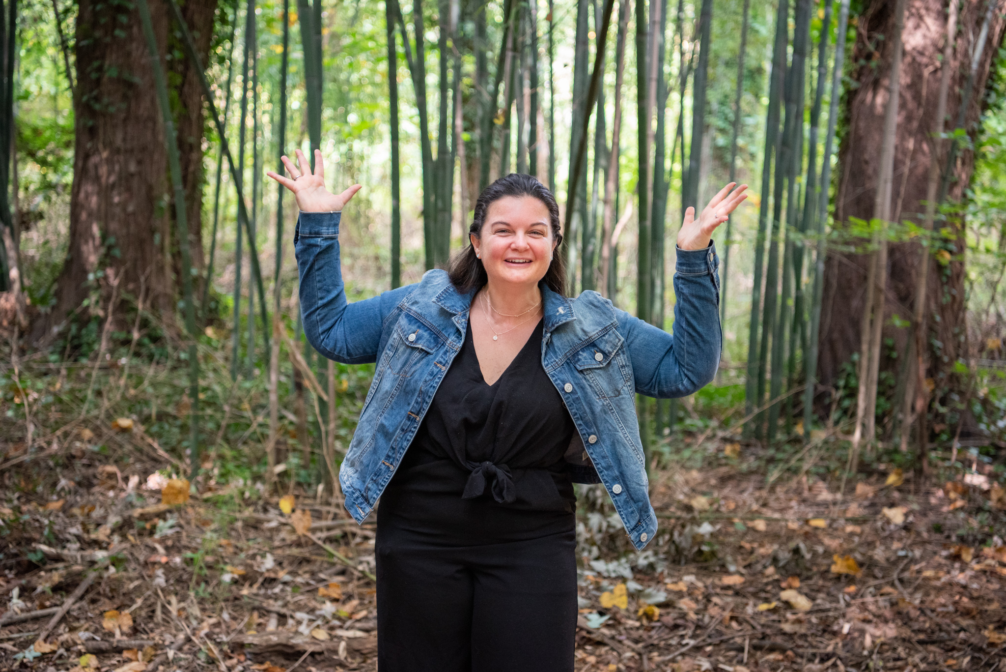 A Caucasian woman holding her hands up like I don't know in a bamboo forest.