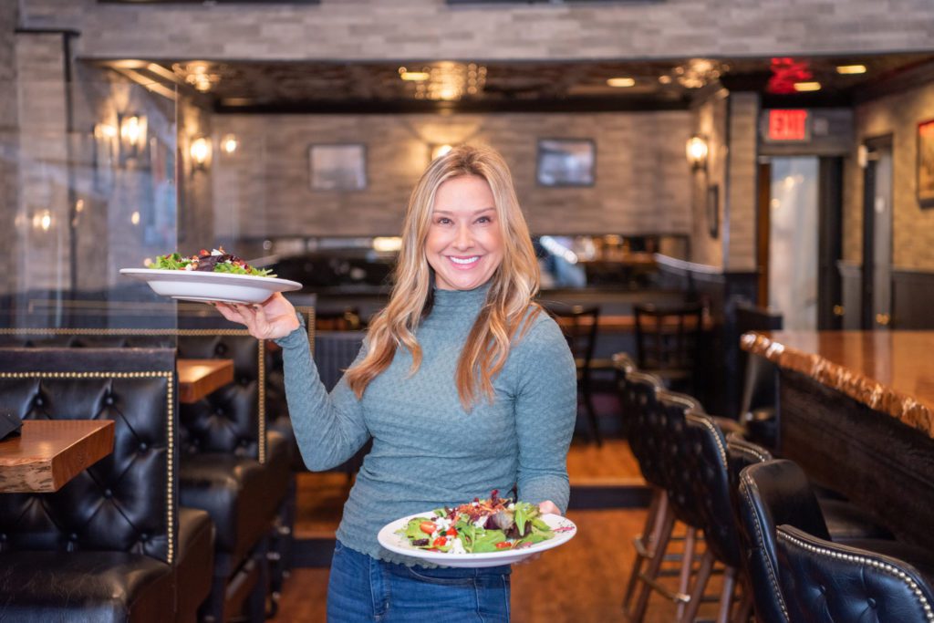 A woman holding 2 plates of salad in Glen Rock Inn, Glen Rock, New Jersey.