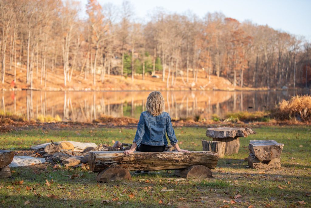 A female public speaking coach taking a break sitting on a log and enjoying the beautiful lake.