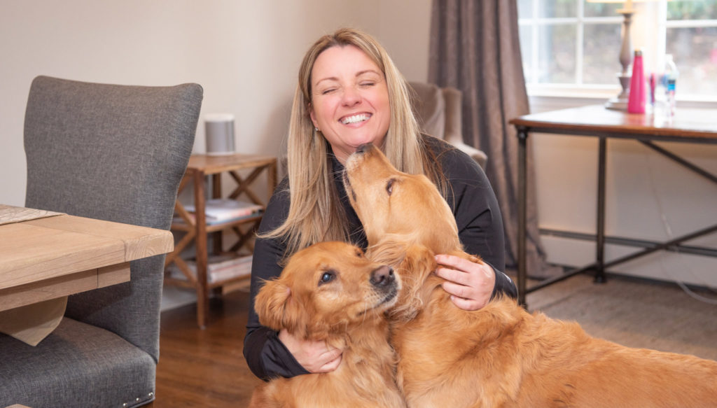 A female social media marketer hugging and getting kissed by her two golden retrievers.