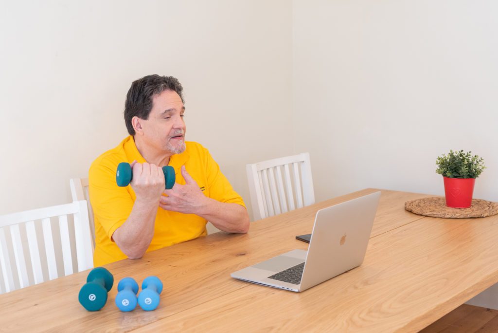 A male health and wellness coach showing his client how to use hand weights on the video conference.