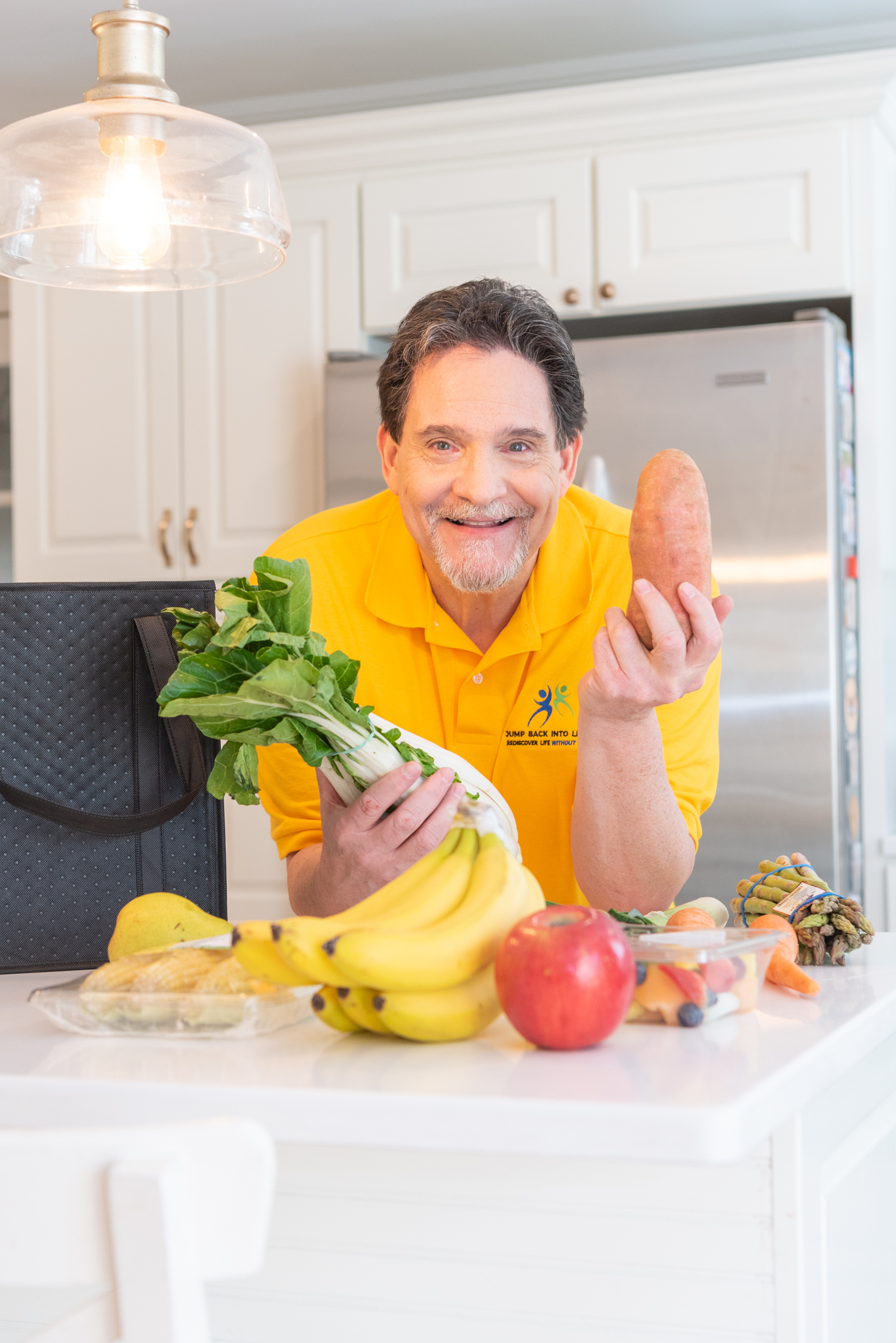 A male health coach with lots of fruits and veggies in his kitchen.
