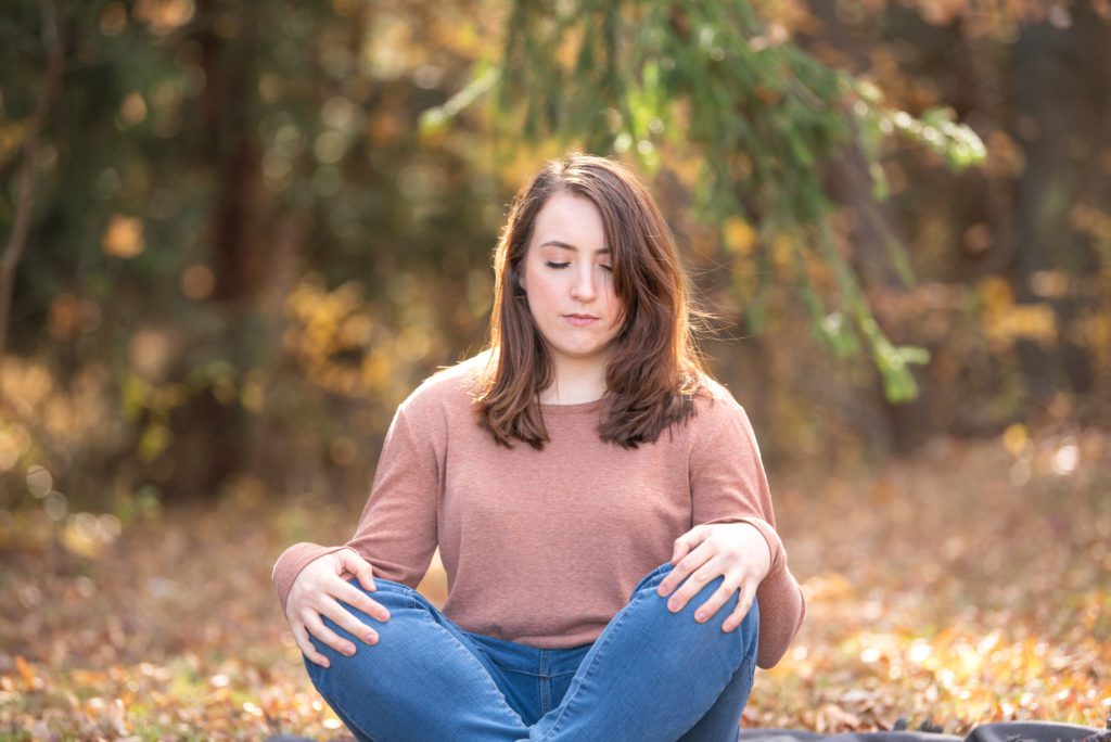 A woman sitting and meditating in the woods.