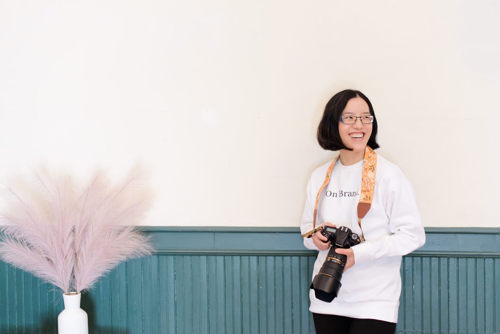 A female branding photographer holding her Nikon D750 DSLR camera in a room.