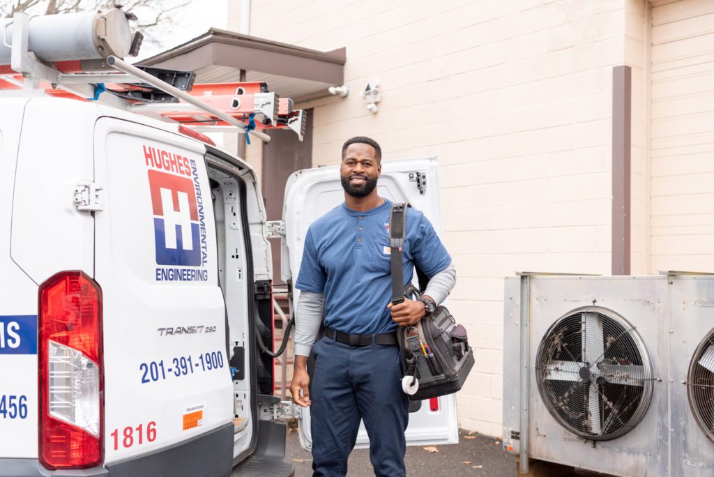 An African American male HVAC technician standing next to his HVAC truck.