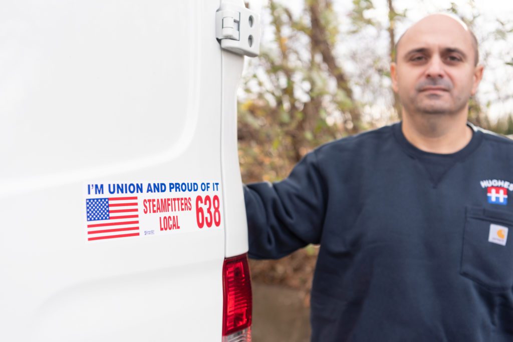 A male HVAC technician showing his "I'm Union and Proud of it" sticker at the back of his HVAC truck.