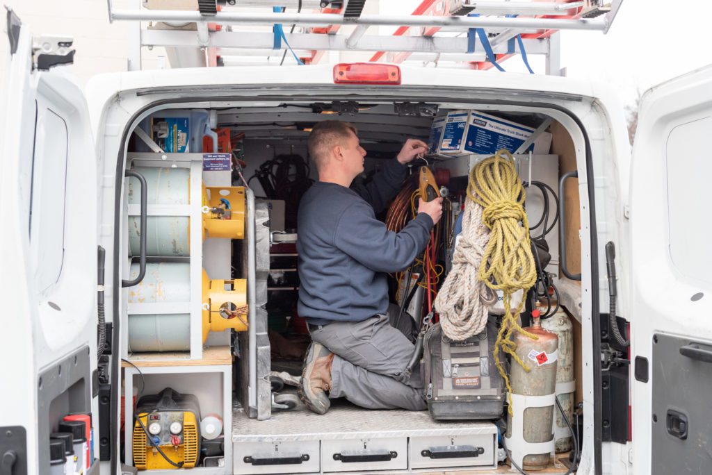 A male HVAC technician getting his tools in the back of his HVAC truck.