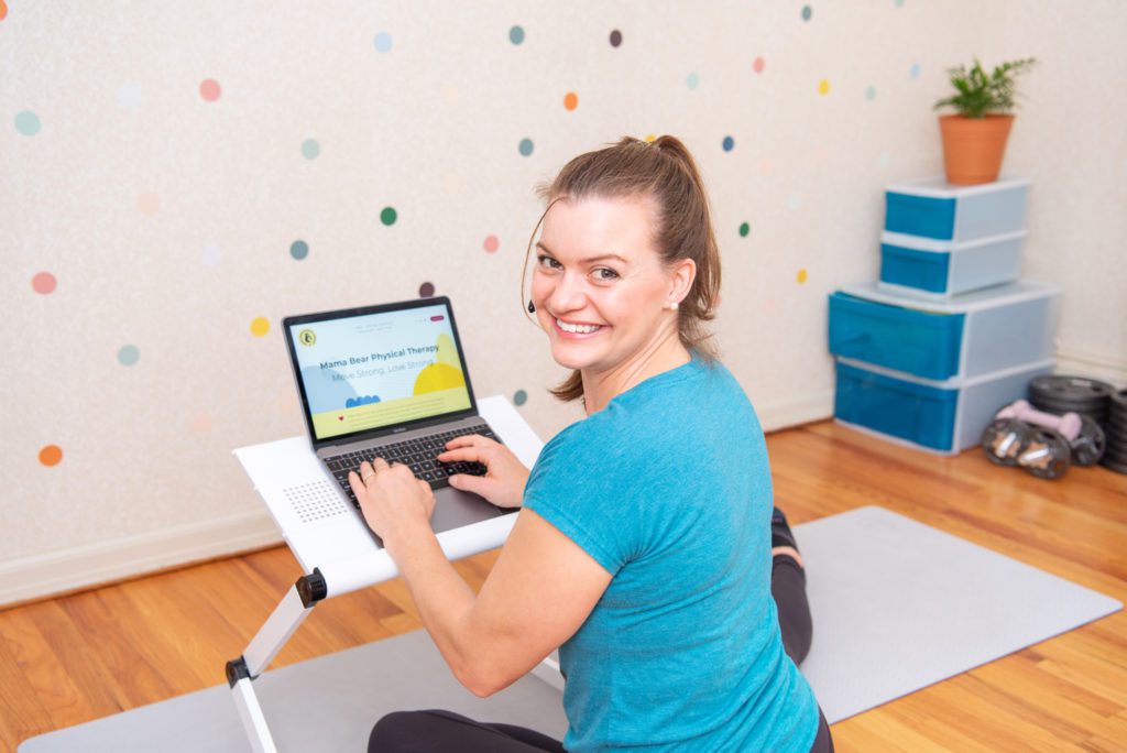 A female orthopedic and pelvic health physical therapist smiling and on her laptop.