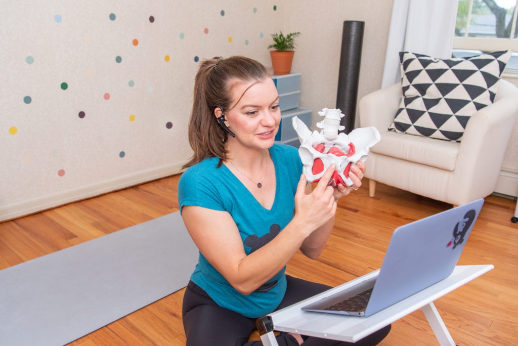 A female orthopedic and pelvic health physical therapist holding a pelvic model in front of her laptop to discuss about pelvic health.