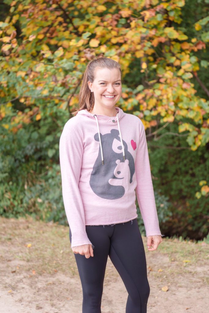 A female orthopedic and pelvic health physical therapist wearing her Mama Bear Physical Therapy branded pink sweatshirt at a park during the Fall season.
