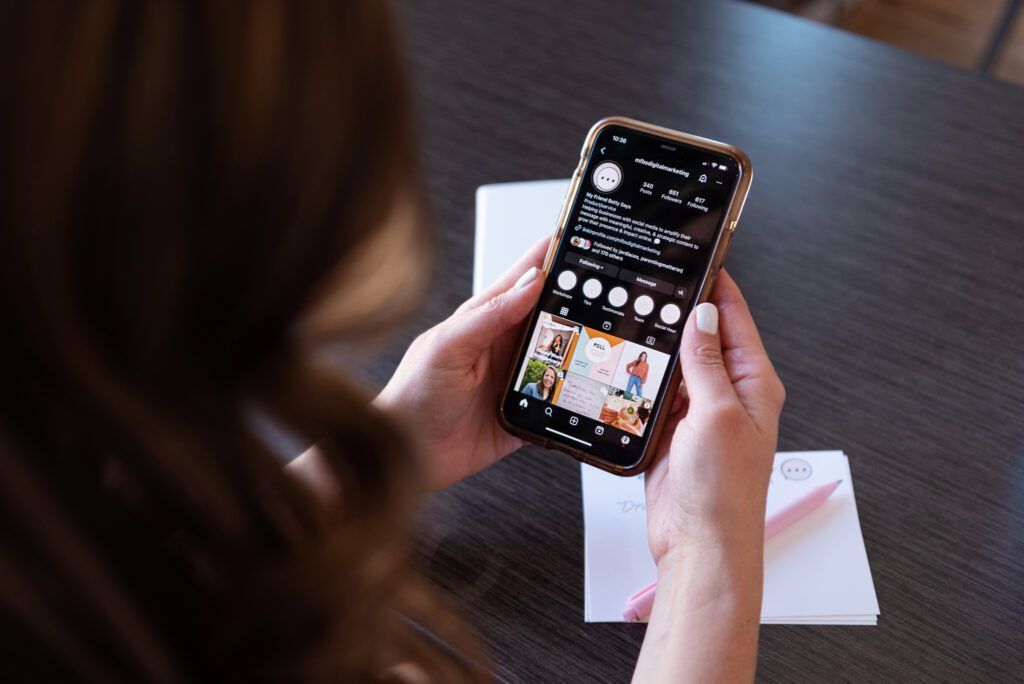 A Latino CEO woman in a brown dress holding her phone and looking at her Instagram profile.