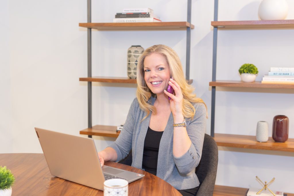 A female online business manager talking to her client on the phone and on her computer in a conference room.
