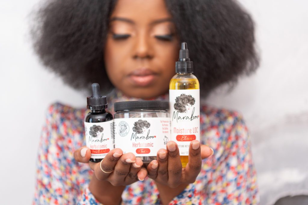 An African American woman holding a line of natural hair care products.