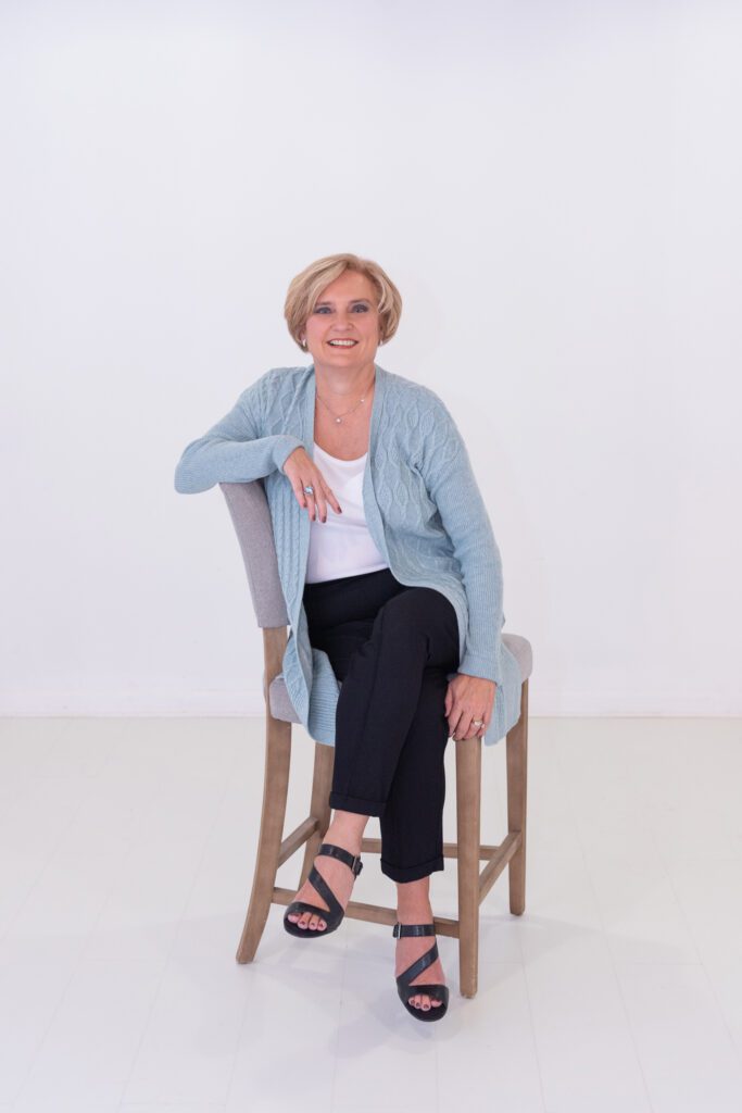 A female health and wellness coach sitting on a high cushion chair posing for her headshot.