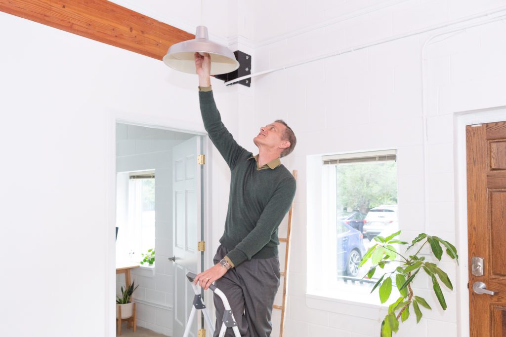 A man standing on a ladder to change a light bulb.