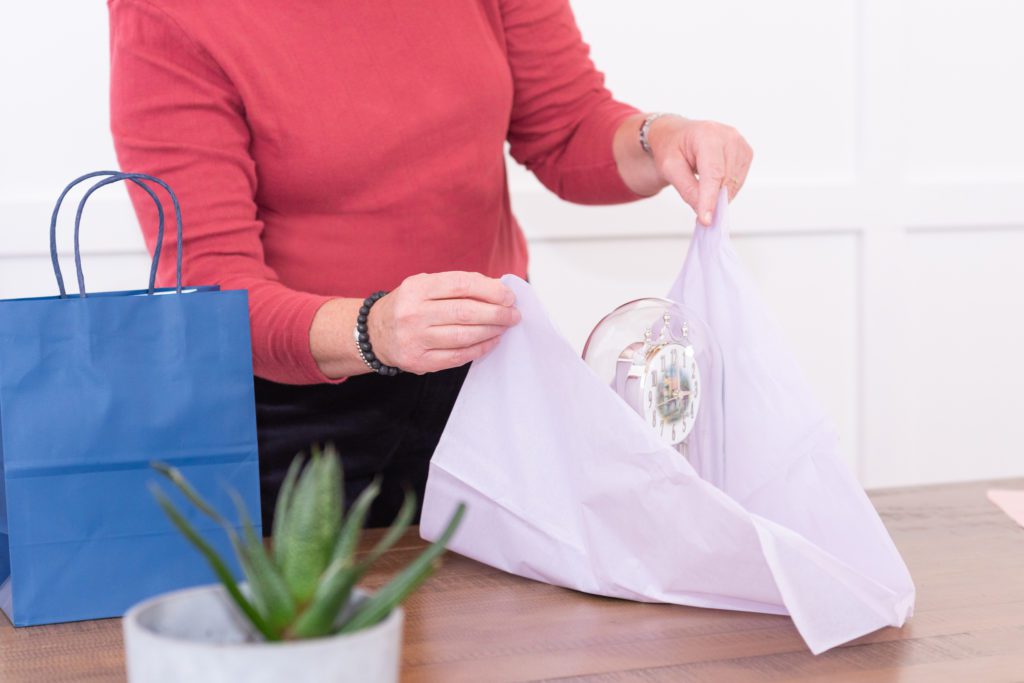 A gift shopper wrapping a clock with tissue paper for her client.