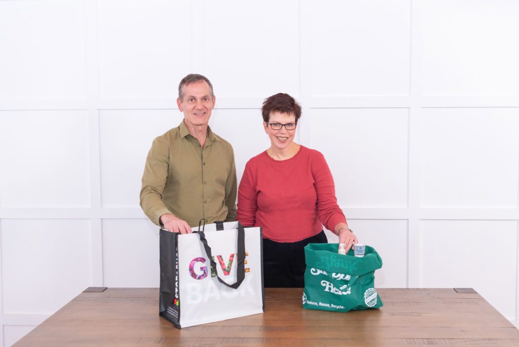 A man and a woman smiling with grocery bags on the dining room table.
