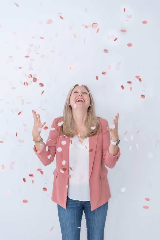 A woman smiling and throwing pink and white confetti in the air.