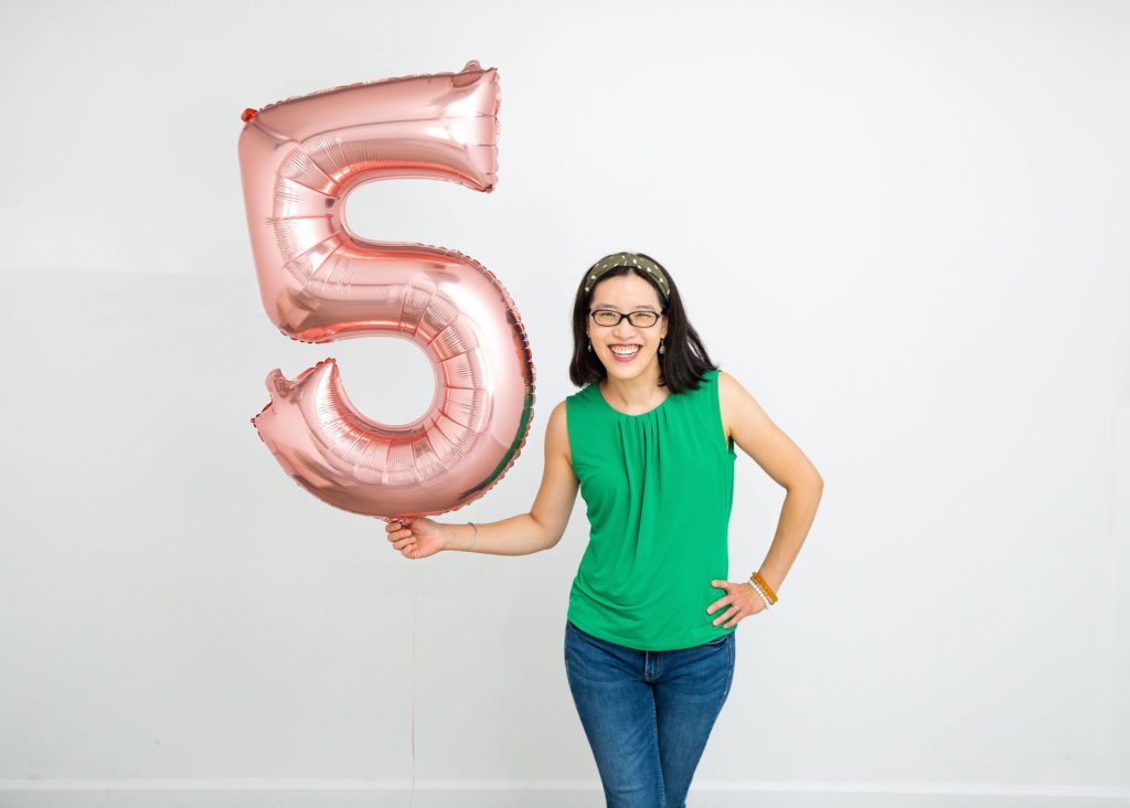 An Asian female holding a number 5 rose gold balloon.
