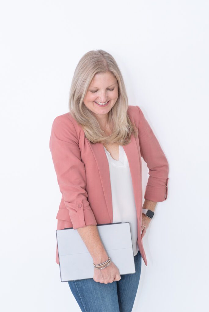 A female business coach holding her laptop and smiling.
