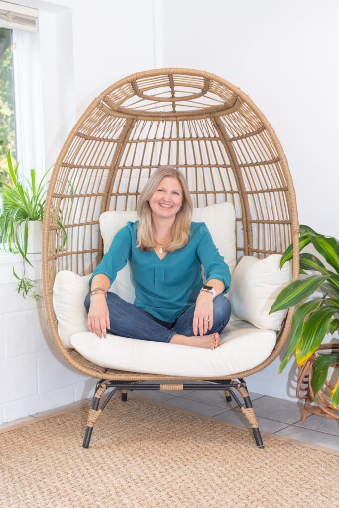 A female business coach smiling and sitting with her legs crossed in an egg chair.