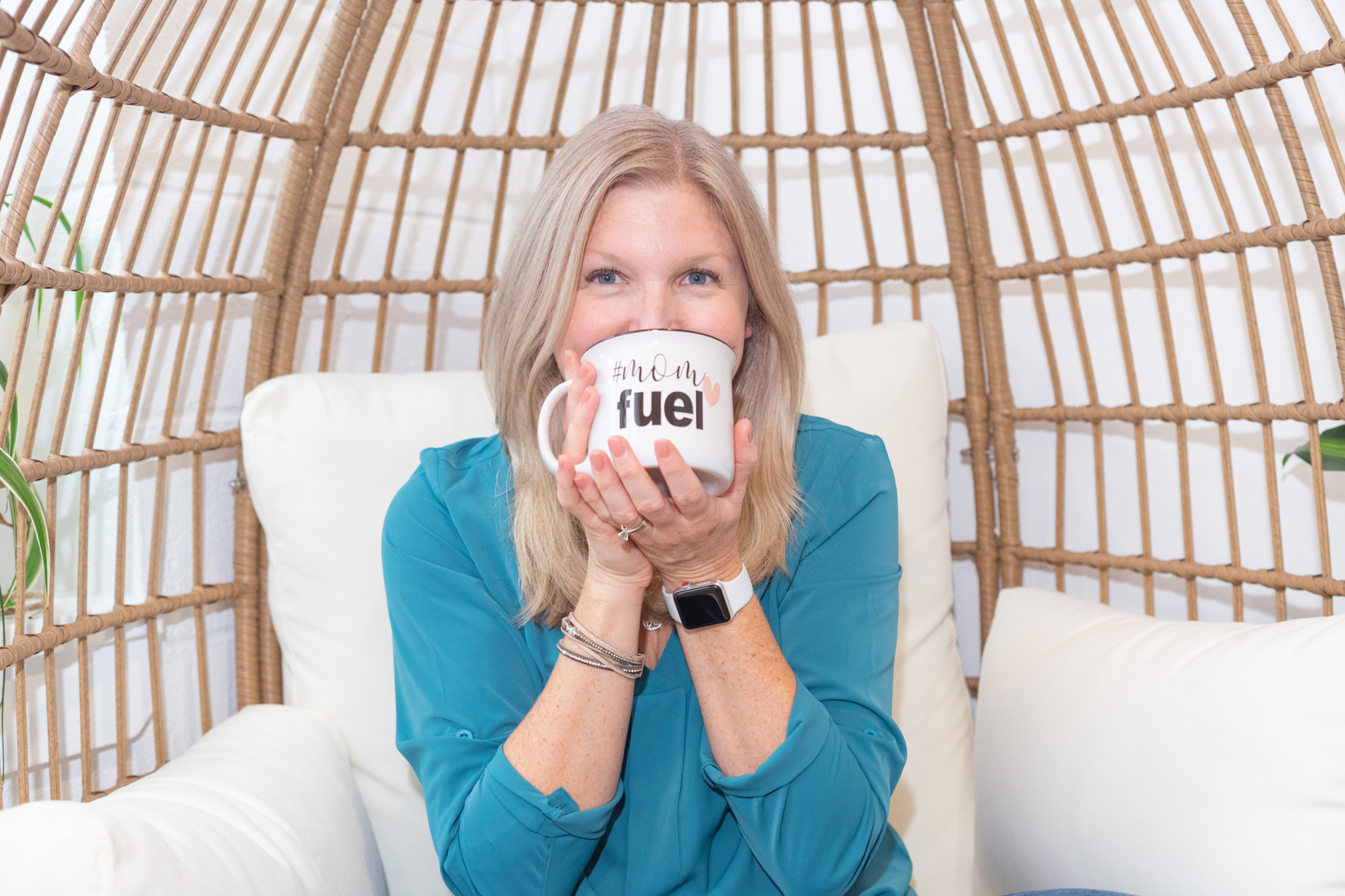 A female business coach sitting in an egg chair and drinking from a mug with "Mom Fuel" text.