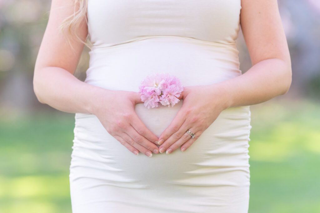 A woman making a heart in front of the pregnant belly with some flowers.