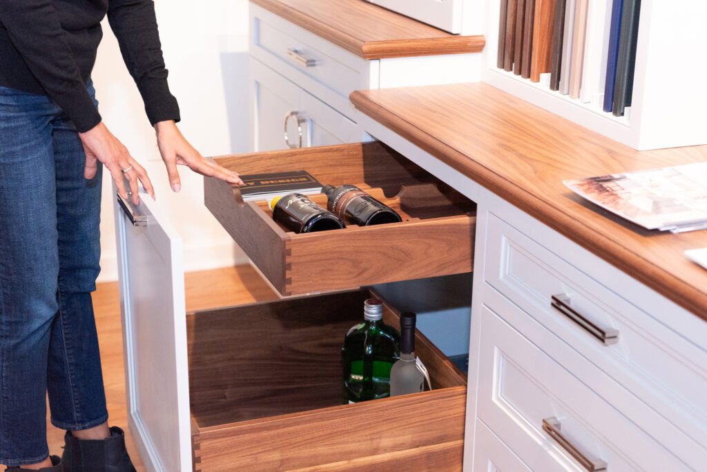 A woman opening a drawer that holds wines and alcohol.