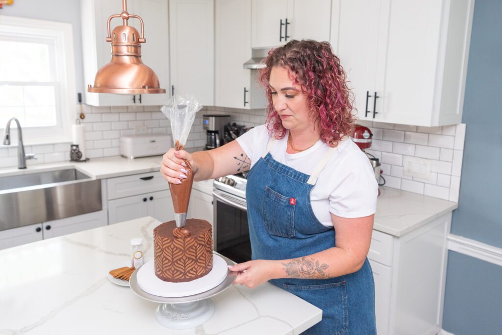 A female New Jersey cottage baker decorating a chocolate cake in her home kitchen.