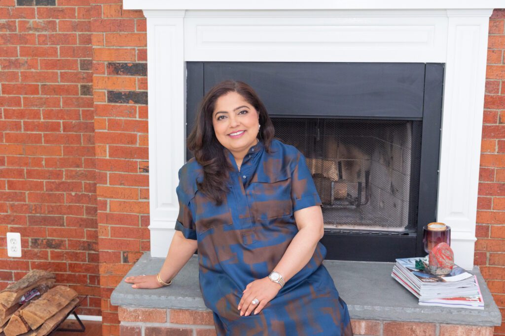A female award-winning jewelry designer smiling and sitting in front of her fireplace.