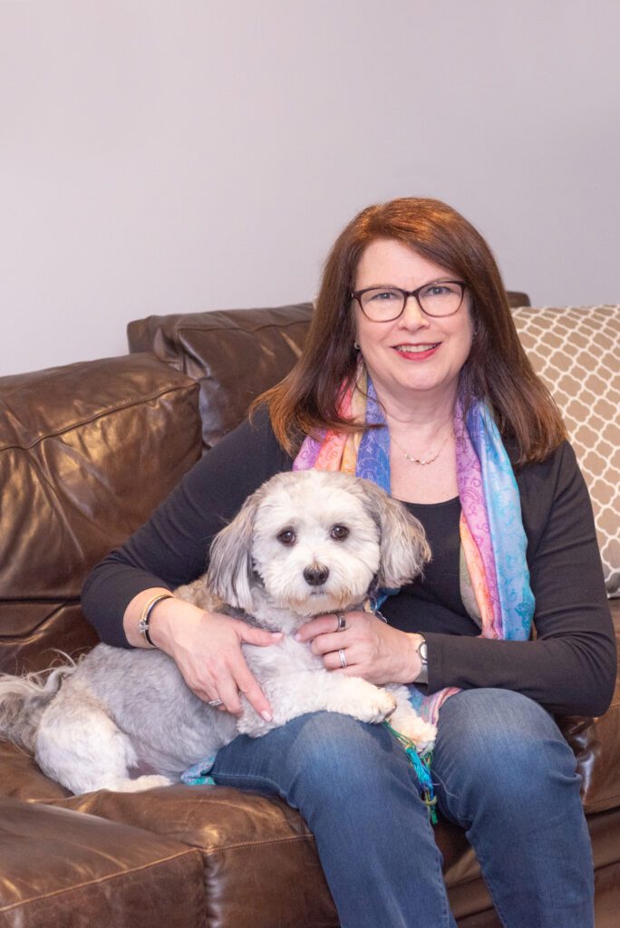 A female professional organizer sitting on a brown couch with one of her pet dogs.