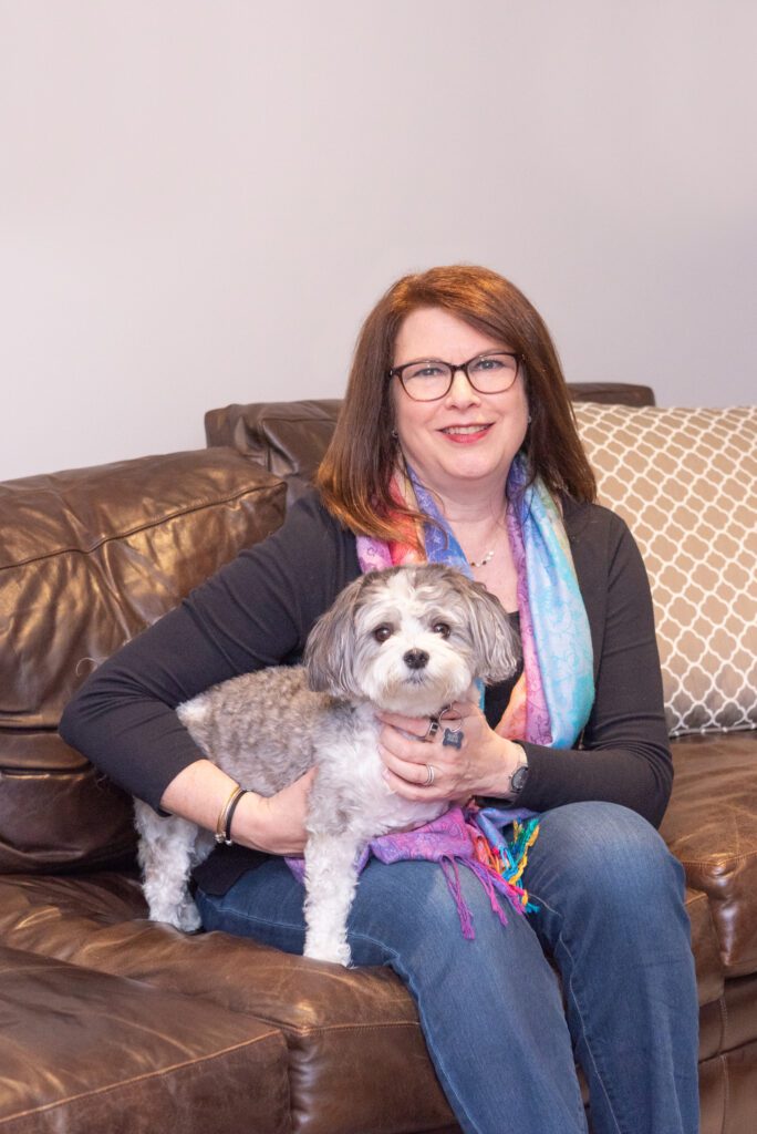 A female professional organizer sitting on a brown couch with one of her pet dogs.