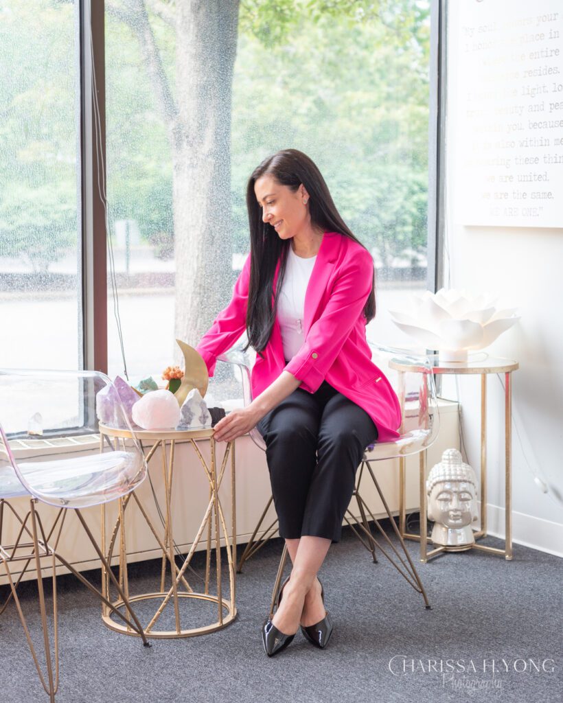 A female Clinical Social Worker and Therapist sitting and touching her crystals with a bright pink blazer.