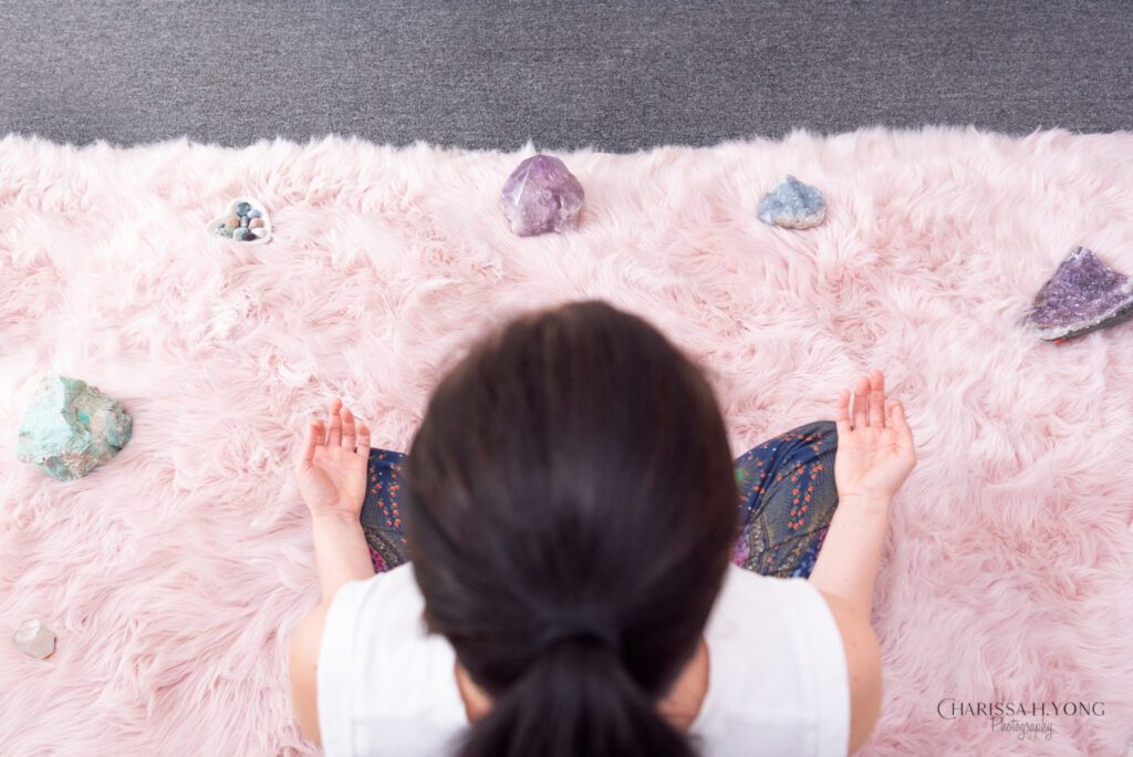 A female Clinical Social Worker and Therapist sitting and meditating with her crystals surrounding her on the carpet.
