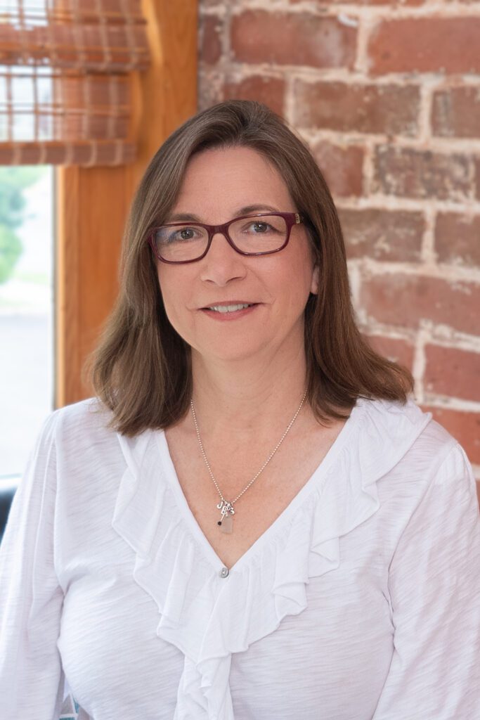 Female CEO of an architecture with a white blouse posing for her headshot in front of a brick wall and window.