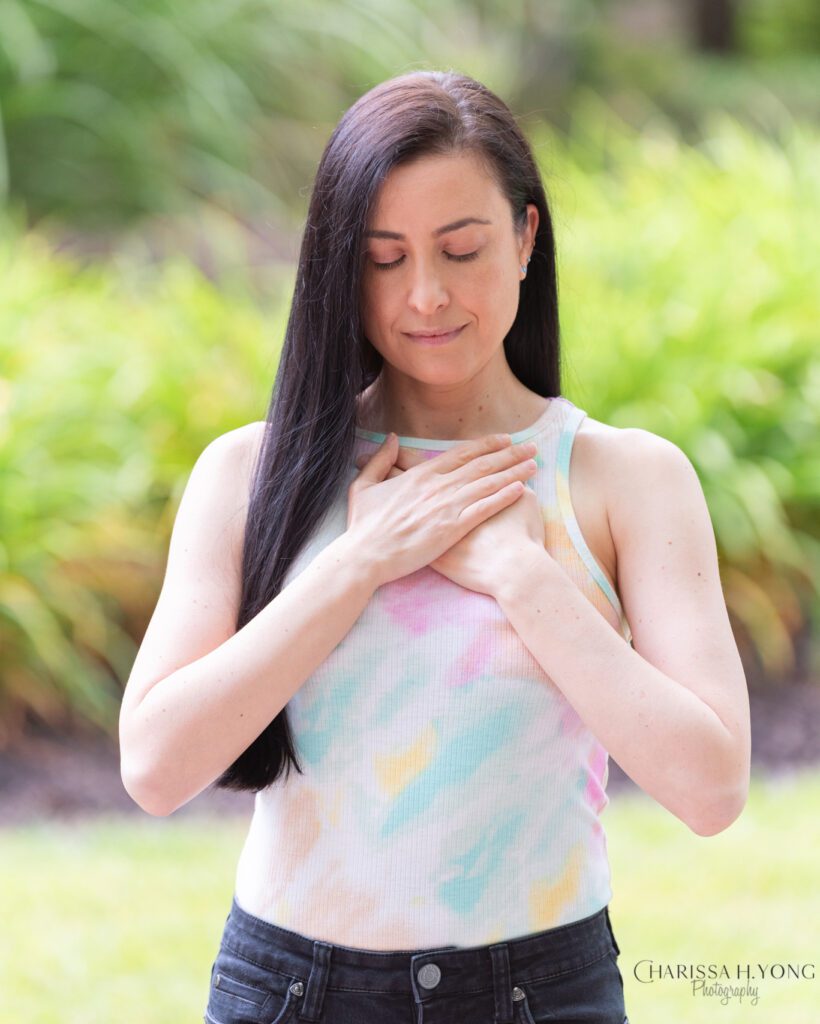 A female Clinical Social Worker and Therapist with her eyes closed and her hands on her chest.