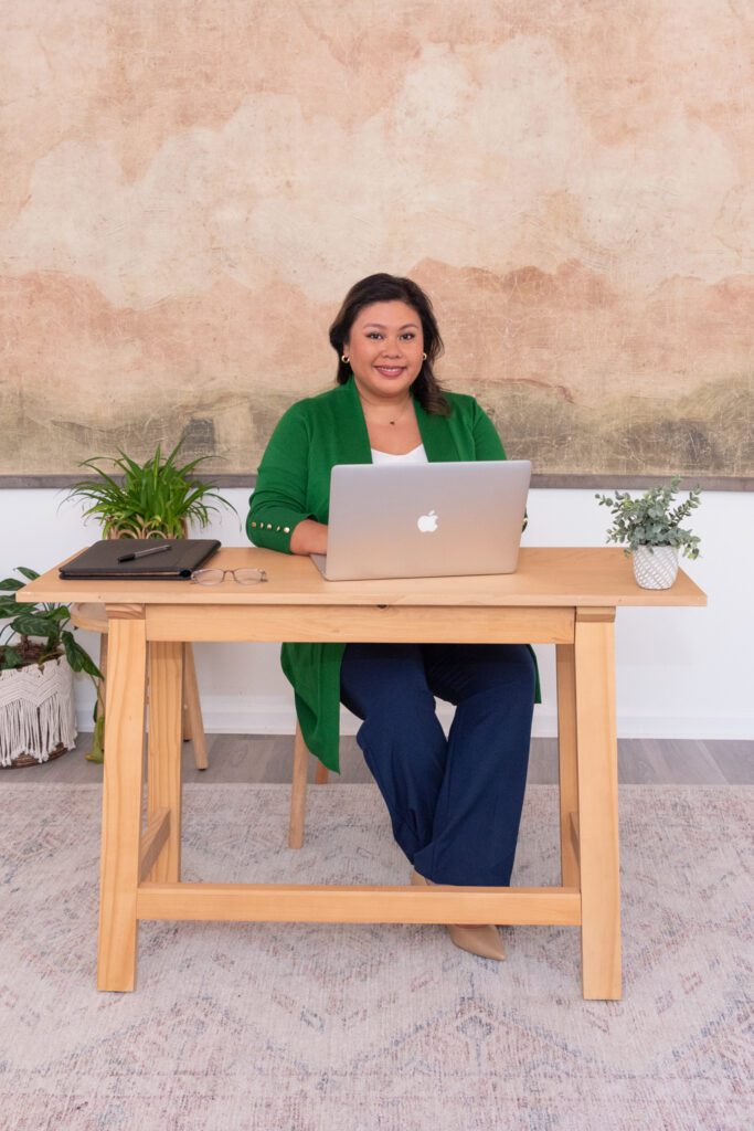 A female CEO of a business consulting company sitting and smiling in her office.