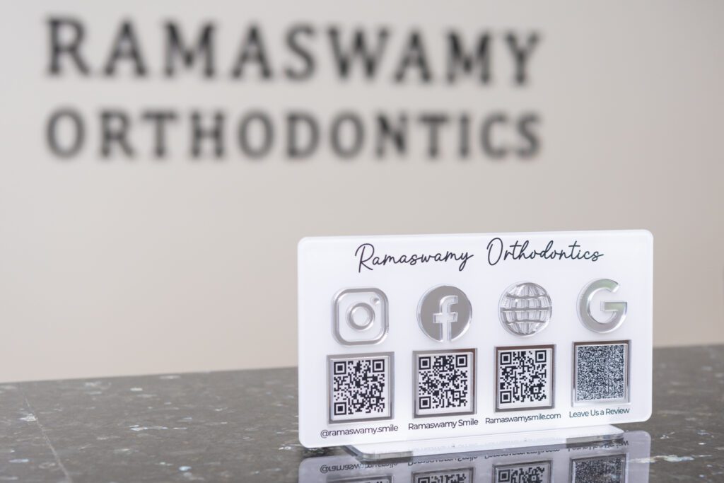 A sign at the Ramaswamy Smile Orthodontics office with social media and website QR codes.