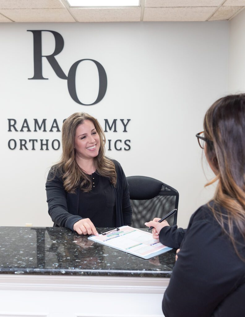 A female receptionist greeting a female patient at the Ramaswamy Smile Orthodontics office.