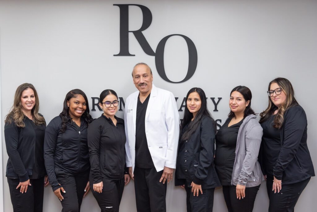 A male board certified orthodontist with his female staff standing in front of their office sign.