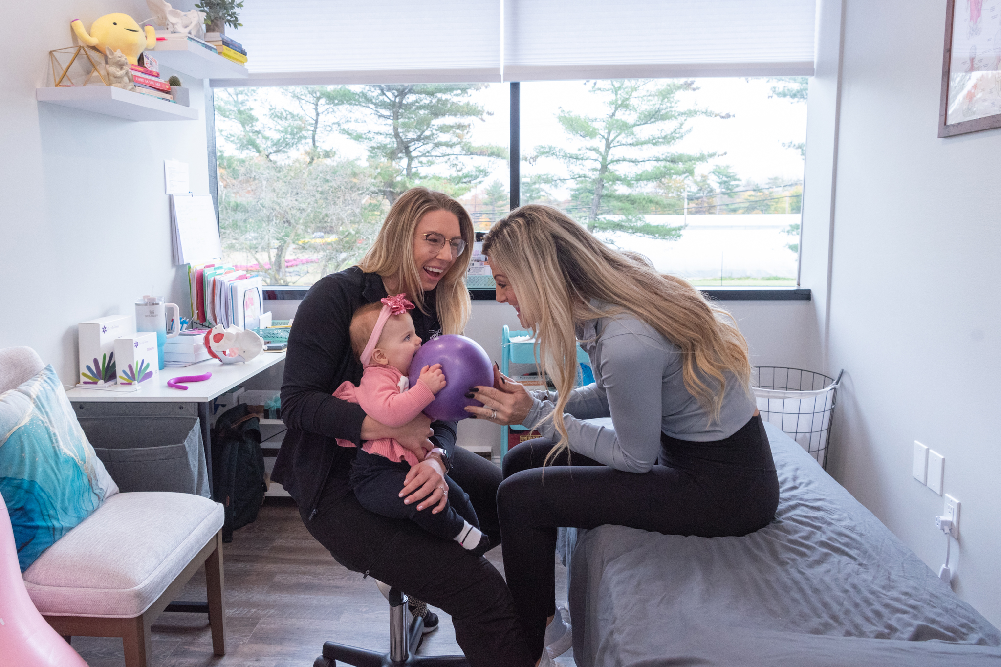 A female pelvic floor physical therapist and her female patient smiling and playing with the patient's infant daughter.