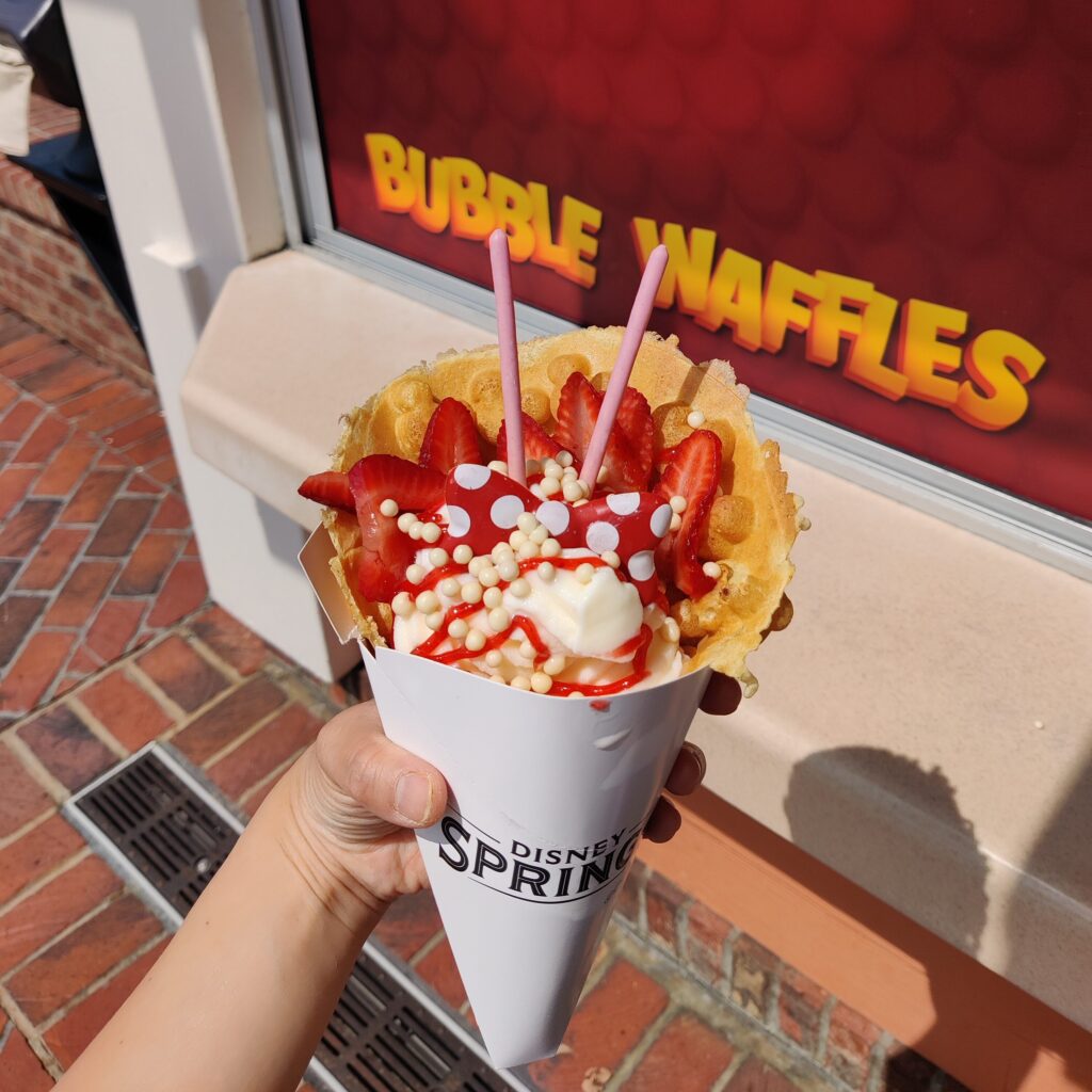 Someone is holding a Mickey bubble waffles with vanilla ice cream and fresh strawberries at Disney Springs, Florida.