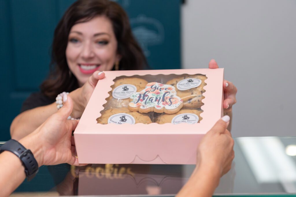 The owner of Treat Me Sweet Cookies in Ridgewood, New Jersey, handing a box of cookies to her customer.