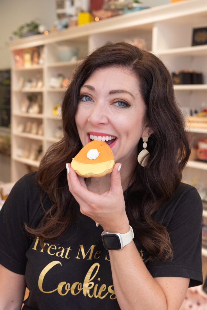 The owner of Treat Me Sweet Cookies in Ridgewood, New Jersey, biting into a pumpkin pie shaped and decorated cookie.