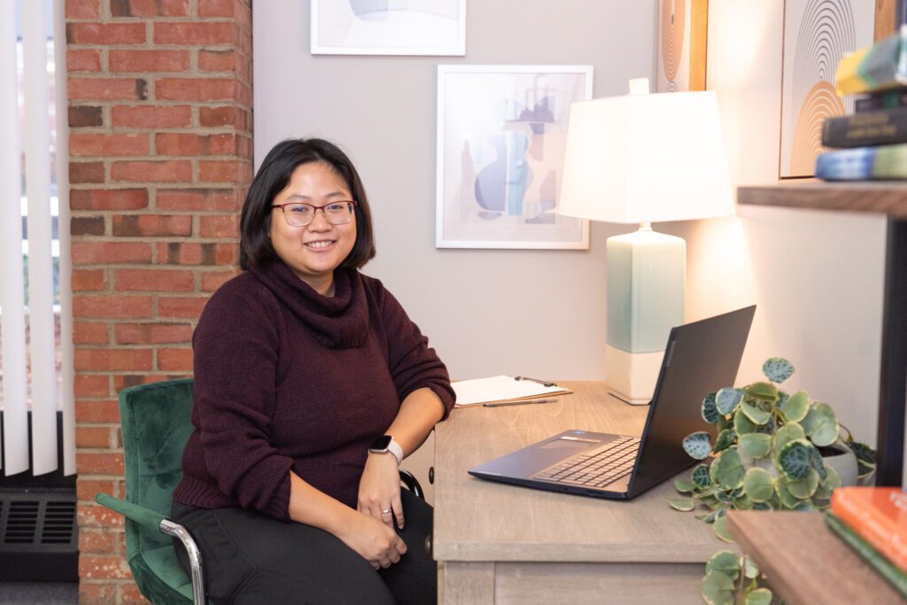 A female therapist sitting with her laptop on a desk in her office.